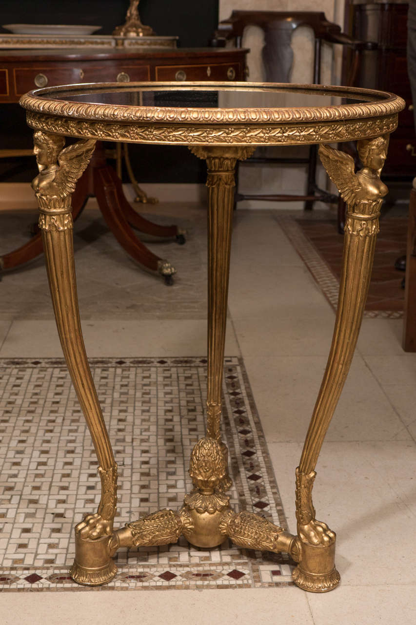 A pair of Art Deco carved giltwood side tables with inset glass pane with winged figural supports.