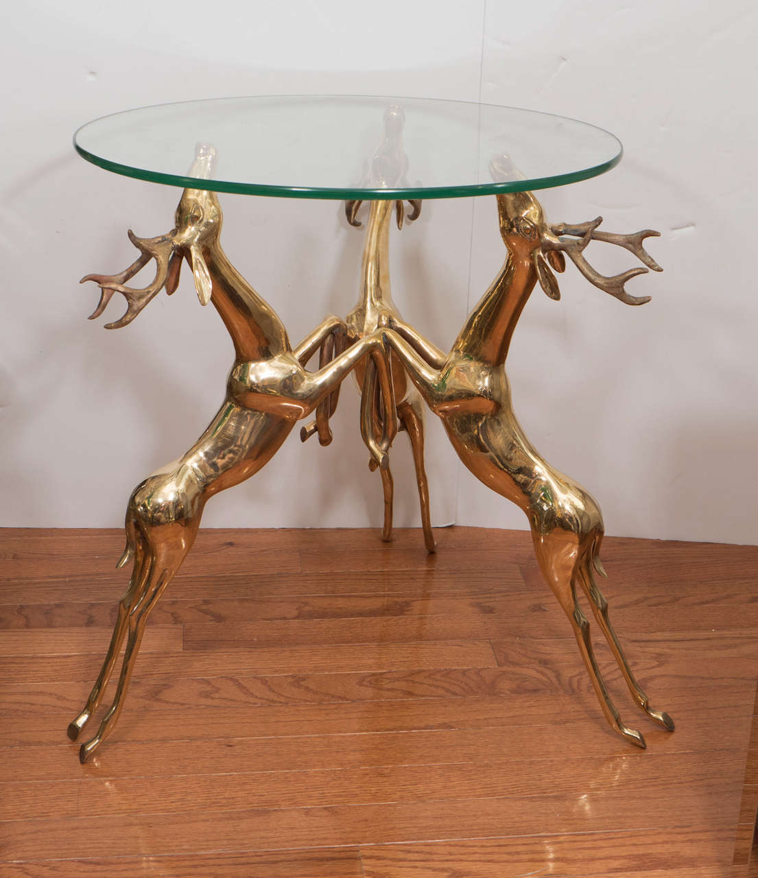 Pair of glass top side tables featuring a brass base composed of a trio of rearing deer. Can be sold individually.