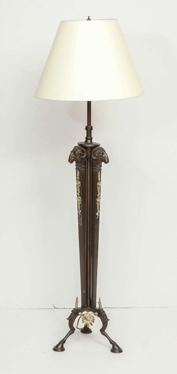 A Danish patinated bronze and brass floor lamp, Circa 1900-10, with a tripod stem headed with Rams heads, foliate and berry cast decoration, raised on a stylized animal leg tripod base. Wired for US electricity. Adjustable height.