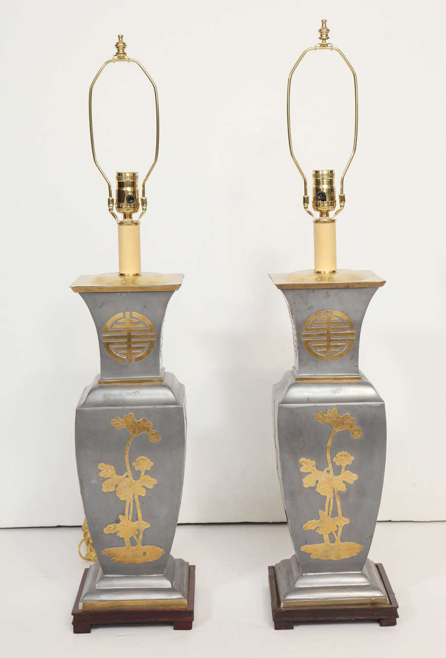 These Chinese motif lamps crafted in pewter grey metal with modernist  Chinese imagery in brass,  sit on hand carved solid wood bases