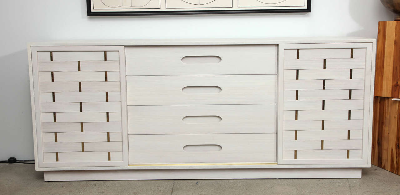 Mid-Century Classic dresser in a bleached/white washed mahogany finish with four ample center drawers and two side compartments concealed by sliding doors featuring woven strips and brass posts. Left compartment has four pull-out drawers, while the