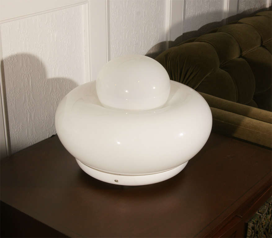 Large glass donut lamp by Vistosi. The lamp has two separate glass pieces that nestle together supported by a white metal base. The lamp has several interior lights operated by a dimmer switch