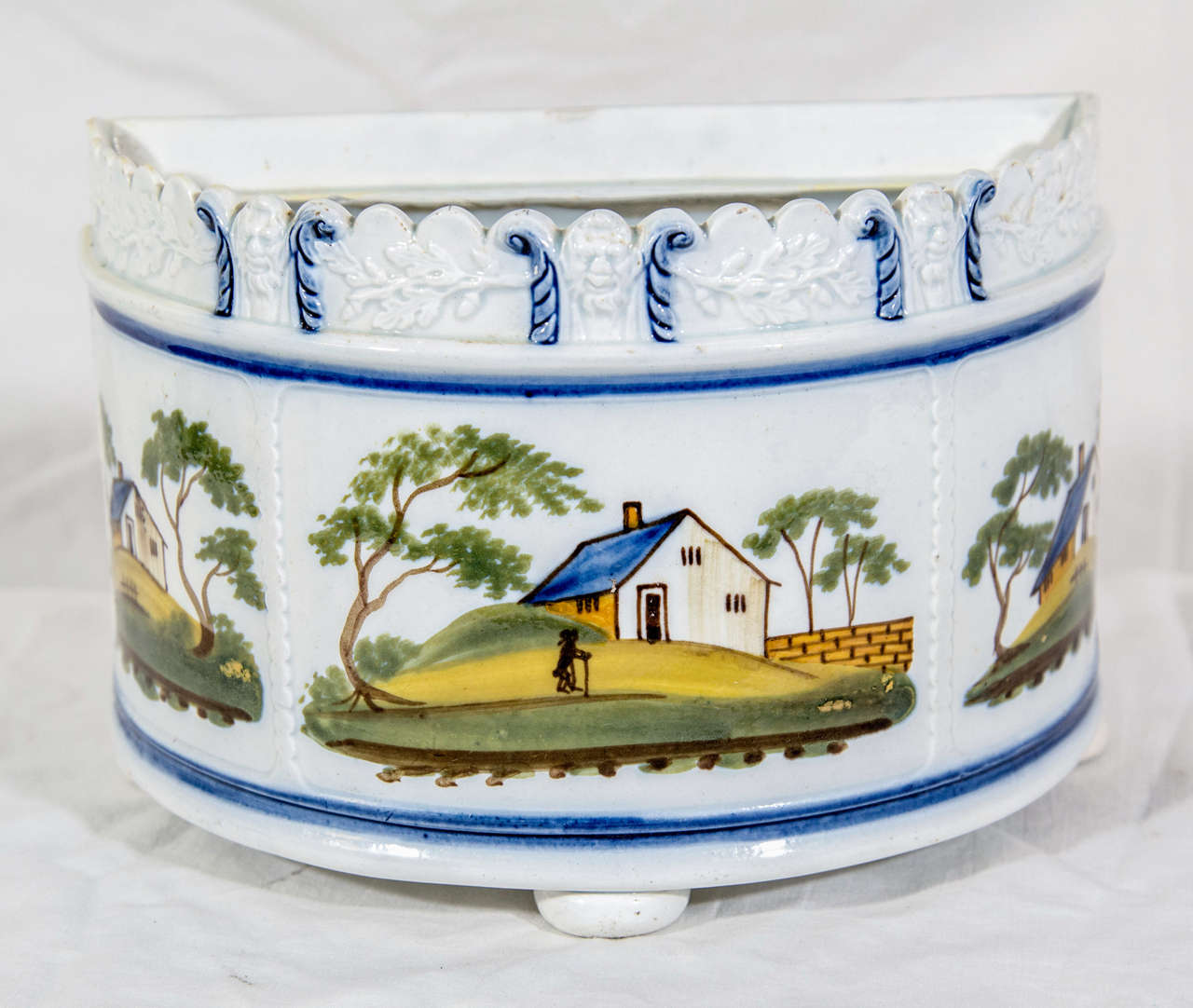A pearlware demi-lune bough pot decorated with naive painted landscapes in Prattware colors,the top rim moulded with masks and branches of oak. It was made in England probably in Yorkshire circa 1815.
Pearlware is a type of creamware to which the