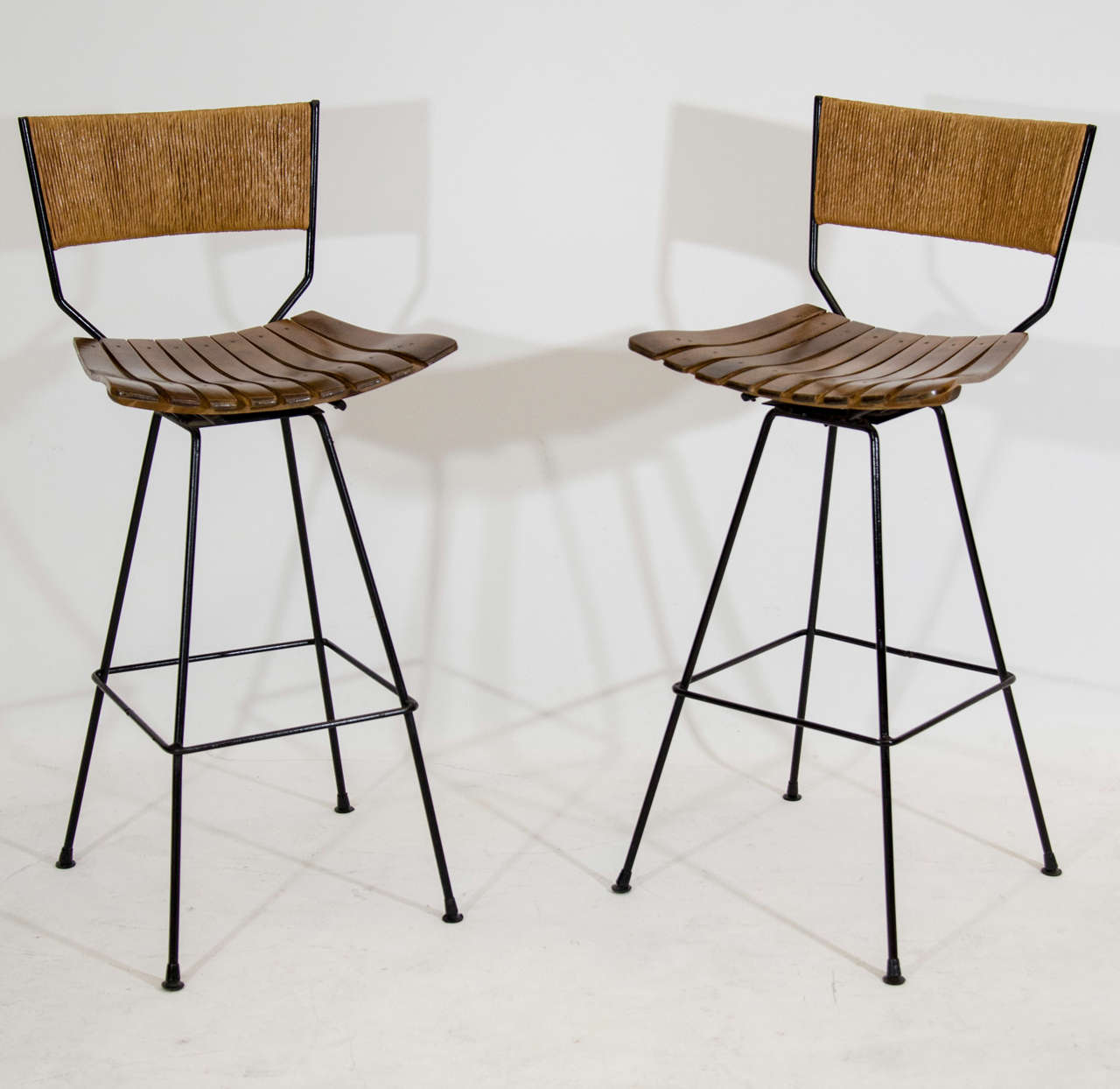 Classic pair of bar stools designed by Arthur Umanoff. The stools swivel and have walnut slatted seats and backrests covered in grass. Please contact for location.