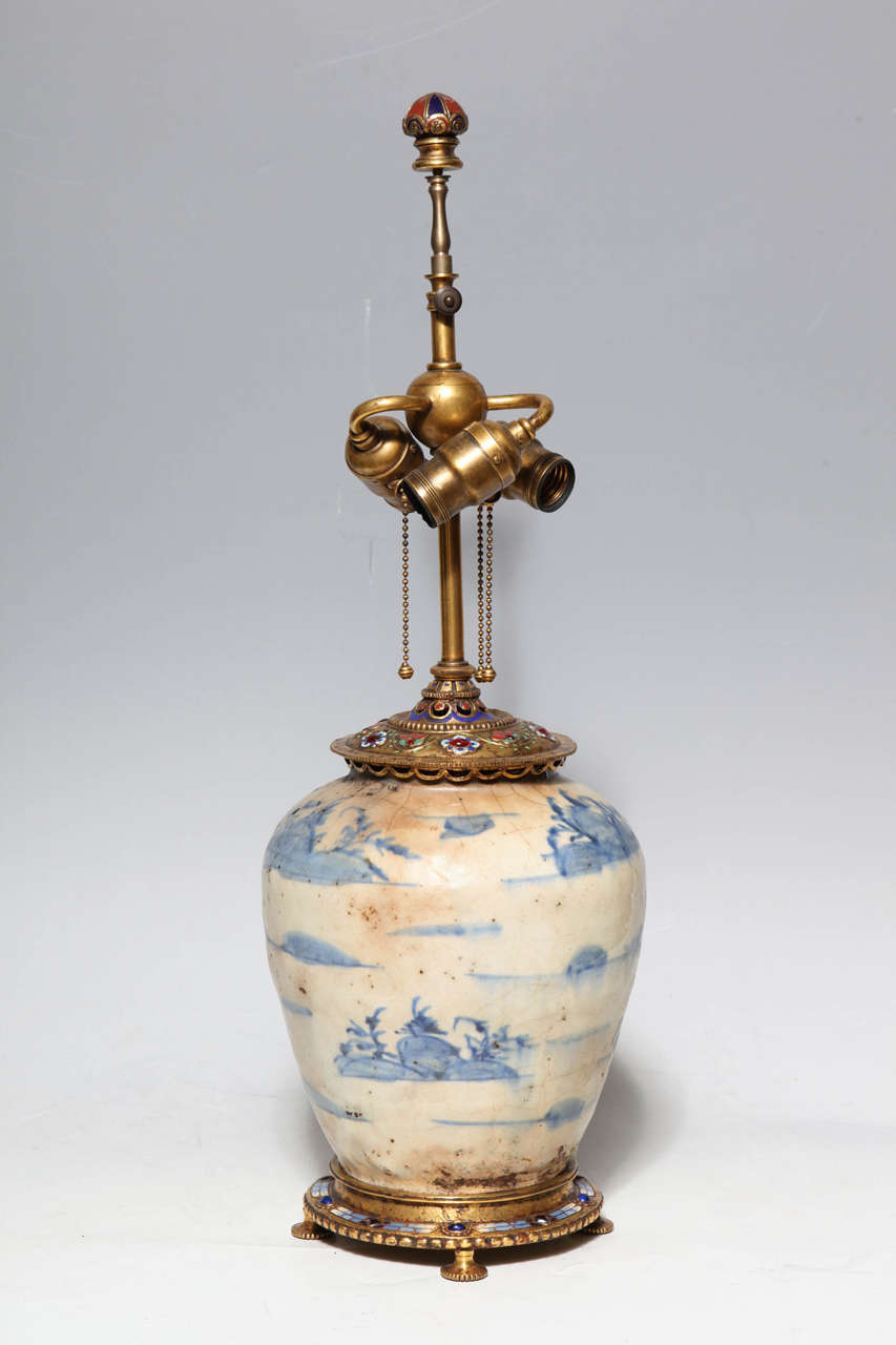 An Ormolu, enamel and jewel mounted Chinese or Korean Porcelain Lamp by E.F. Caldwell. The jewels are elegantly inlaid into the Ormolu mount with enamel coloring complimenting the sparkle of the gems. The blue and cream porcelain is covered with