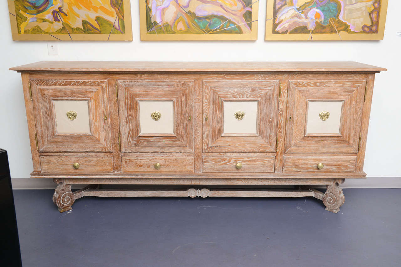 In cerused oak, this piece stands on an elegant carved base.
4 doors .  In each one ,in the middle ,a bronze figure . 
Shelves inside. 4 drawers on the bottom part.