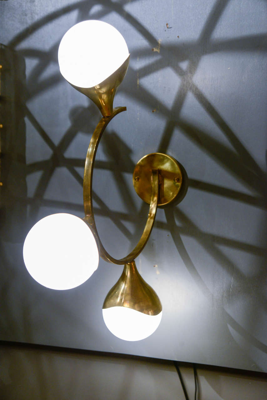 Surprising and very unusual set of six wall sconces made of a curved brass arm going out of the wall and three globes hiding the bulbs.

New electrification.