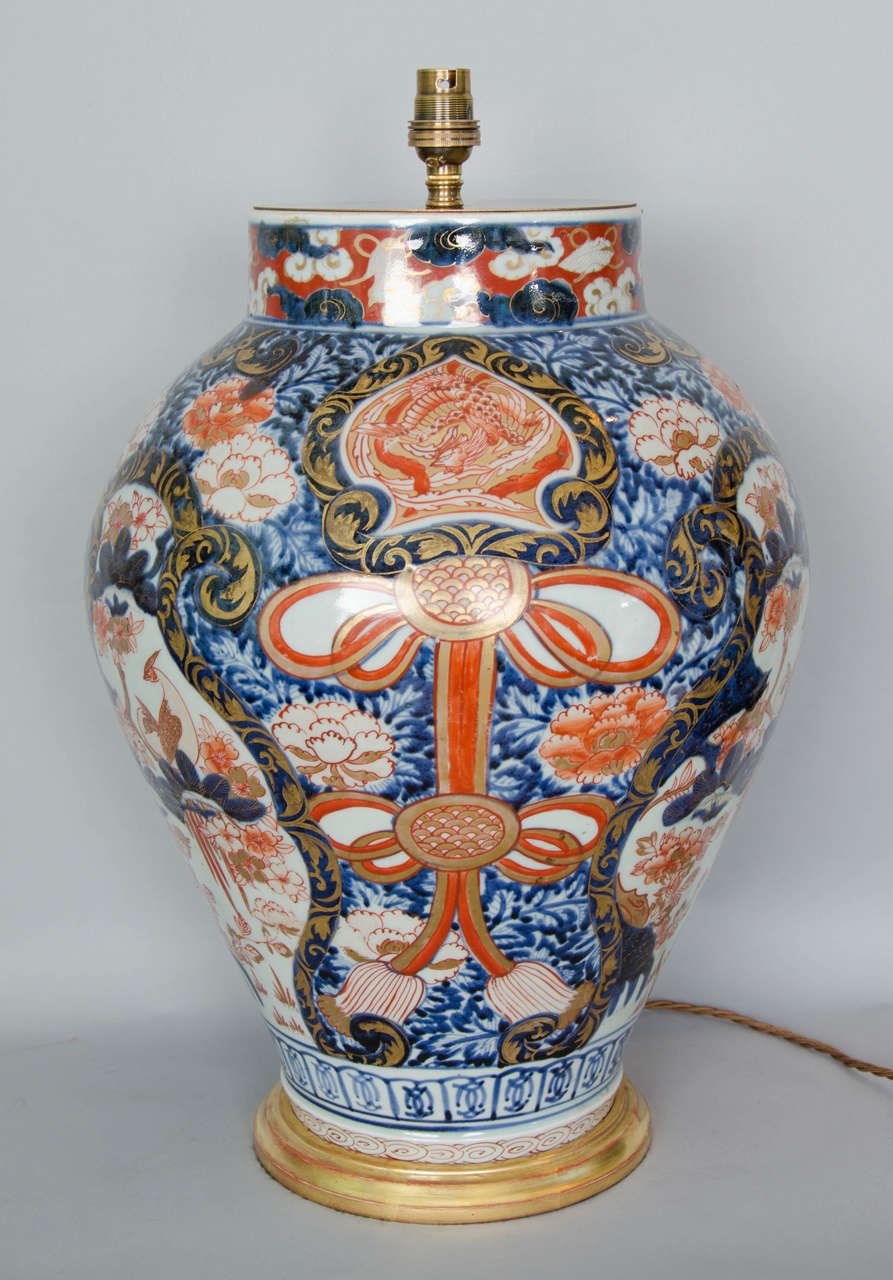 A large Japanese Imari porcelain vase dating around 1700 Lamped with a handcarved and gilted wooden base. 
The decoration is quite elaborate with three big shaped panels depicting phoenixes resting on trees amongst peonies and, between the panels,