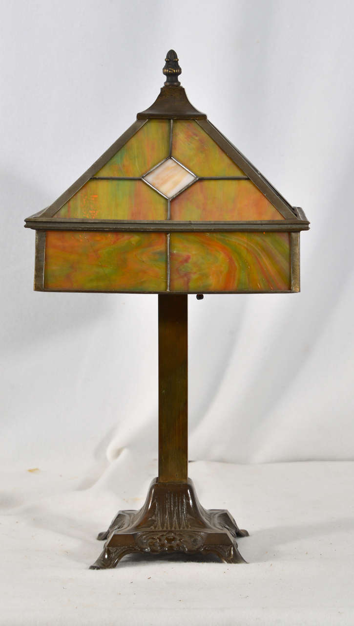 1930'a Arts & Crafts,Leaded  Glass Sshade in muted colors of green, amber, and orange. on a square lamp base, cast bronze base and column.  Lamp has been rewired and is a beautiful example of Arts and Crafts Period.