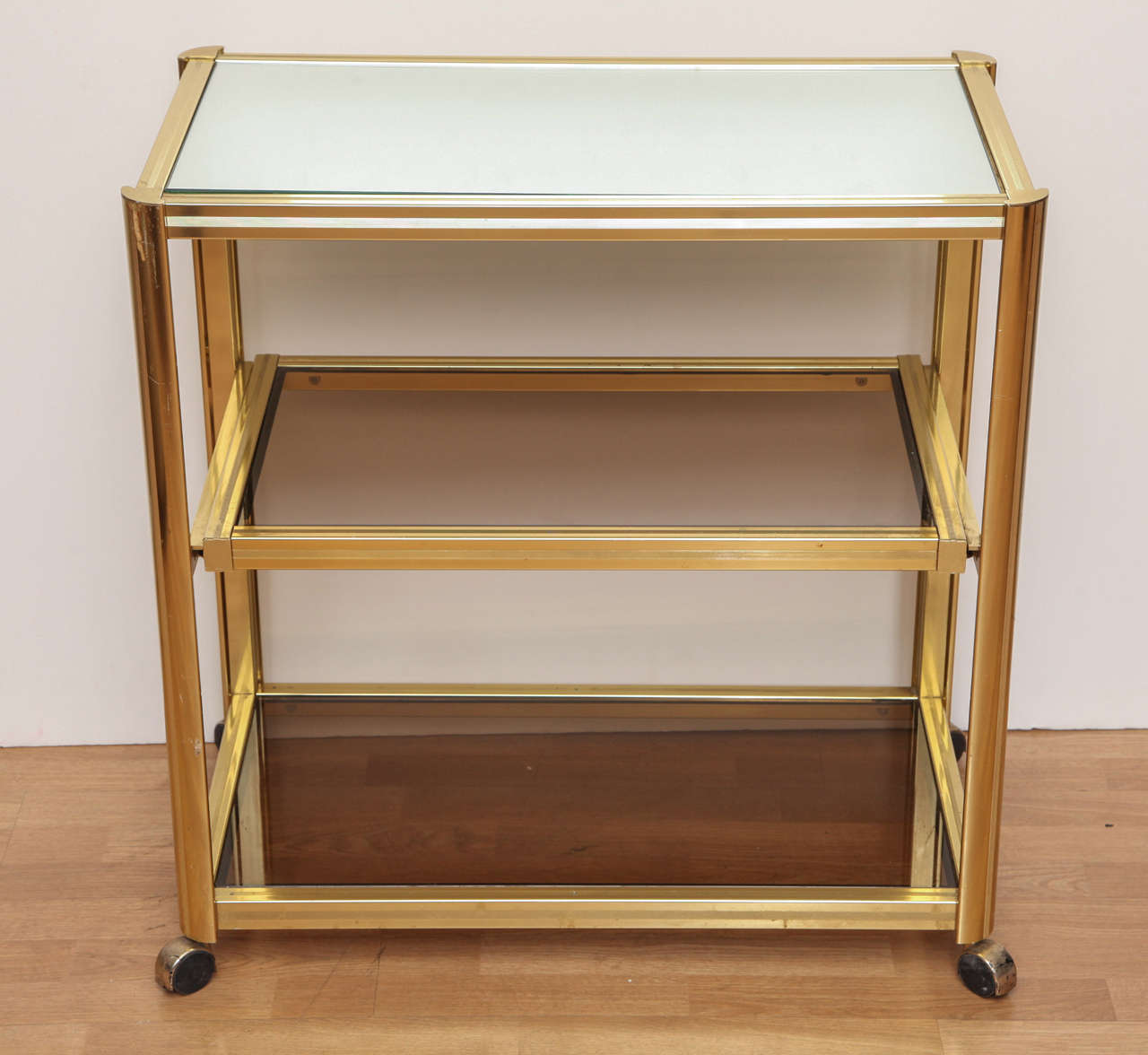 Modernist rolling bar cart in polished brass with mirror top and smoked glass shelves. Middle shelf pulls out; practical for serving.