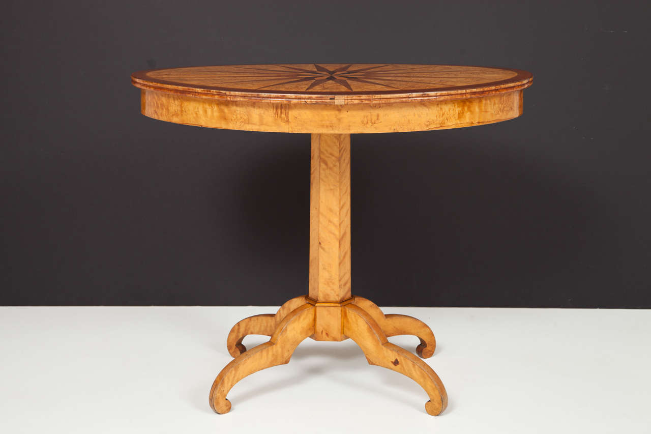 A Swedish birch, birchroot, mahogany and walnut inlaid side table, Circa 1840s, the inlaid oval top raised on a hexagonal stem and four double scrolled legs.

Provenance:
Made in Stockholm around 1840 in the Neoclassical style. It is marked with