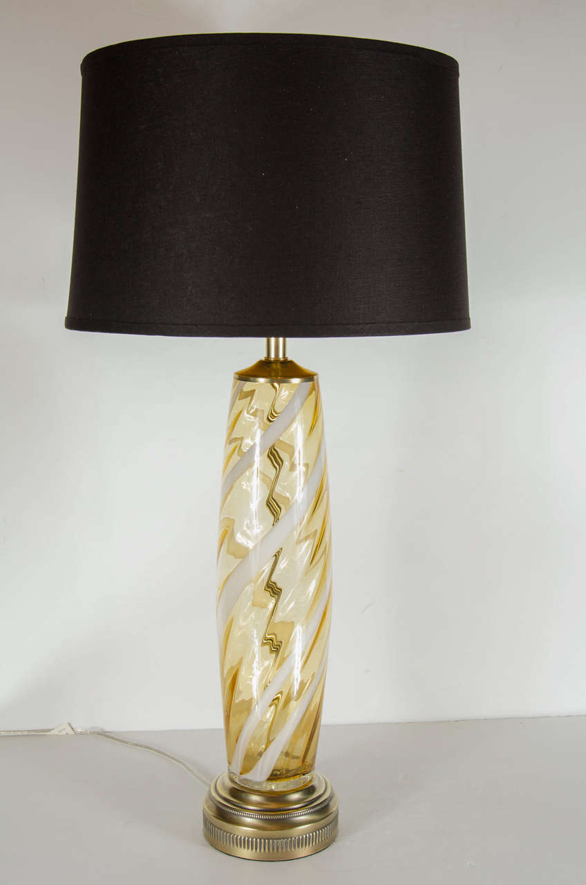 Mid-Century Modern handblown Murano glass table lamp with an accentuated column form featuring amber shaded Murano glass swirled with stripes of white milk glass. It has antique brass fittings and thick antique brass base with stepped, fluted and