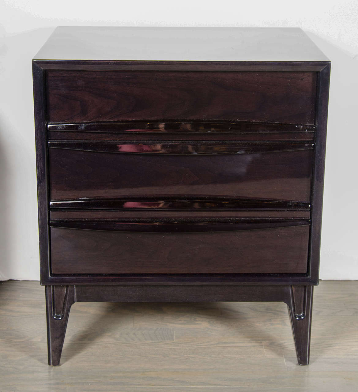This pair of Mid-Century Modern end tables or night stands in the manner of Vladimir Kagan in ebonized walnut feature three drawers with incorporated stylistic pulls and tapered legs. Restored to mint condition.