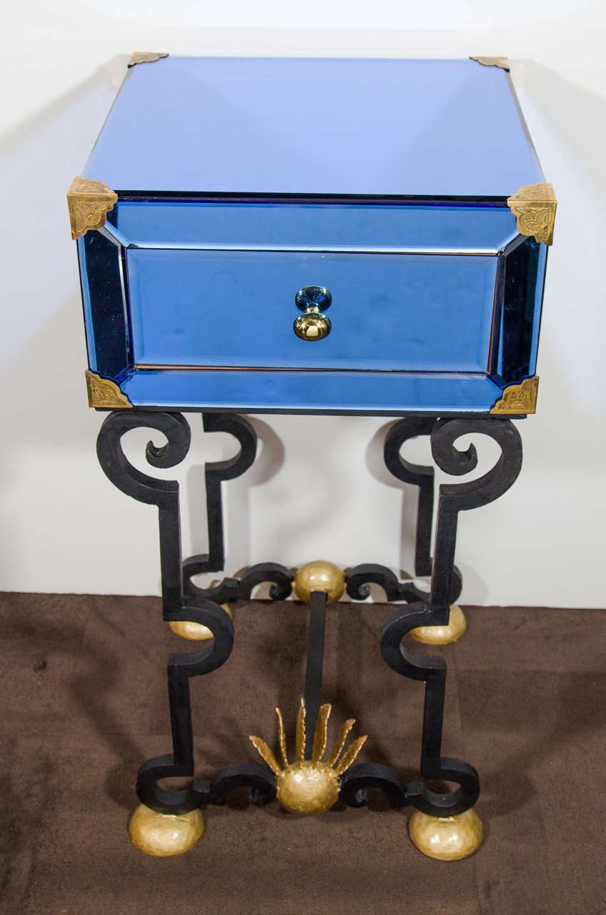 Pair of extraordinary Venetian mirrored end tables with hand forged wrought iron bases. The tables features striking sapphire tinted hand glass with hand beveled details. Each table is fitted with one center drawer and features hammered brass