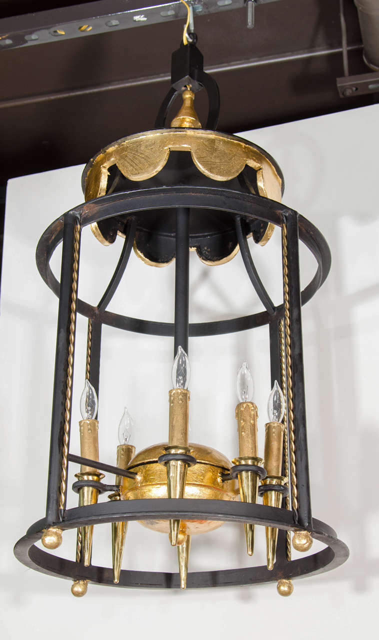 Outstanding wrought iron chandelier with architectural lantern design. The chandelier features hand applied gold leaf accents over hand forged wrought iron designs.  Highly stylized cage form with gilded braided rope details, gilded center orbital