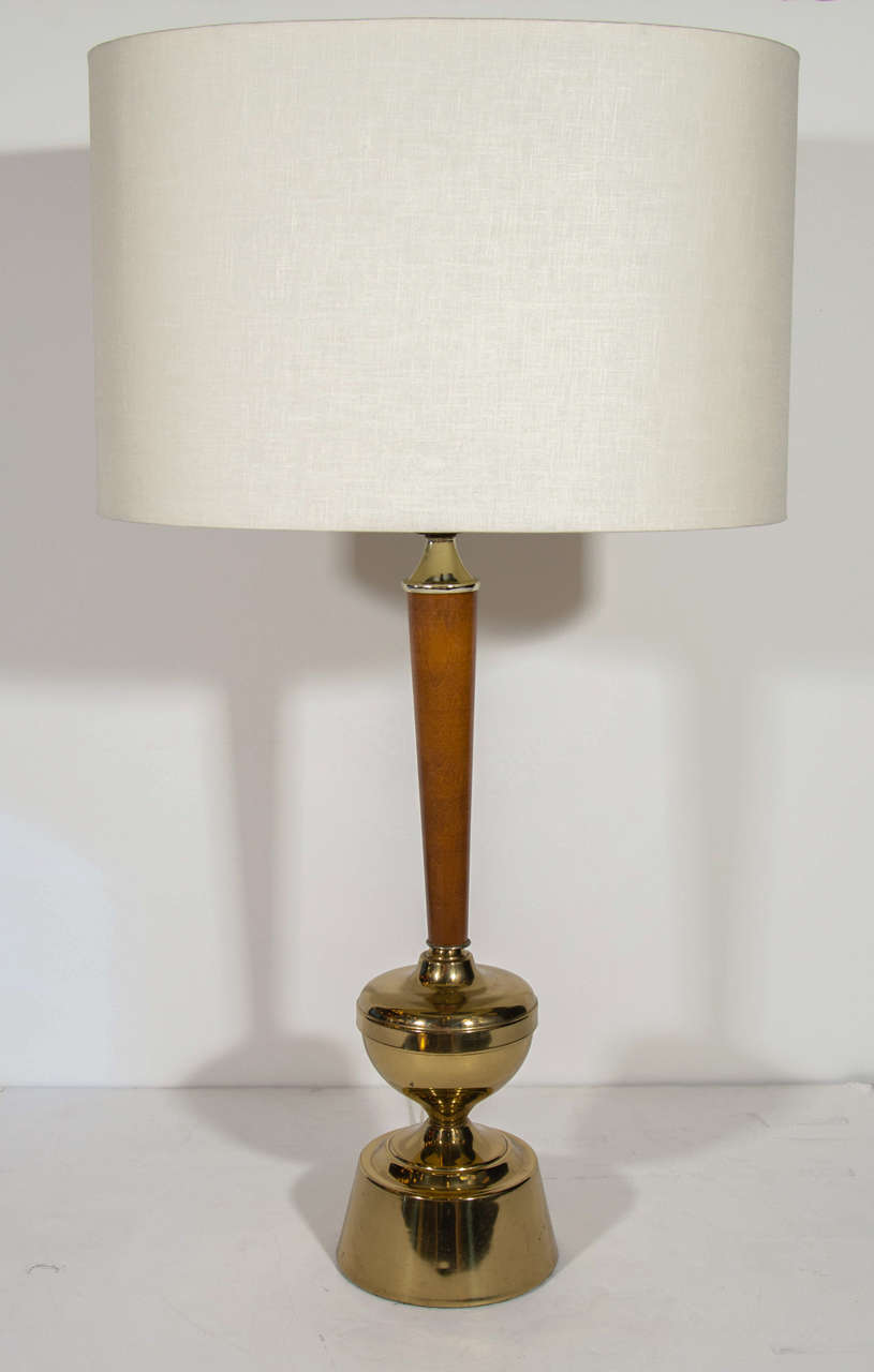 Elegant Mid-Century Modern lamp with a teakwood stem and a turned brass base. The base features an ultra-modern plinth design with a highly stylized hourglass form. The lamp has brass fittings above the stem, and has been newly rewired. Shown with a