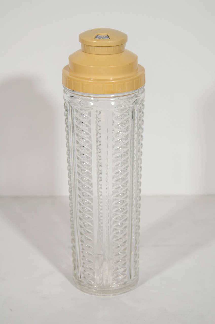 Art Deco era tall barware shaker in glass with vertical faceted glass pattern and fluted details. The shaker features a stepped bakelite top with Machine Age inspired design that also functions as a strainer.