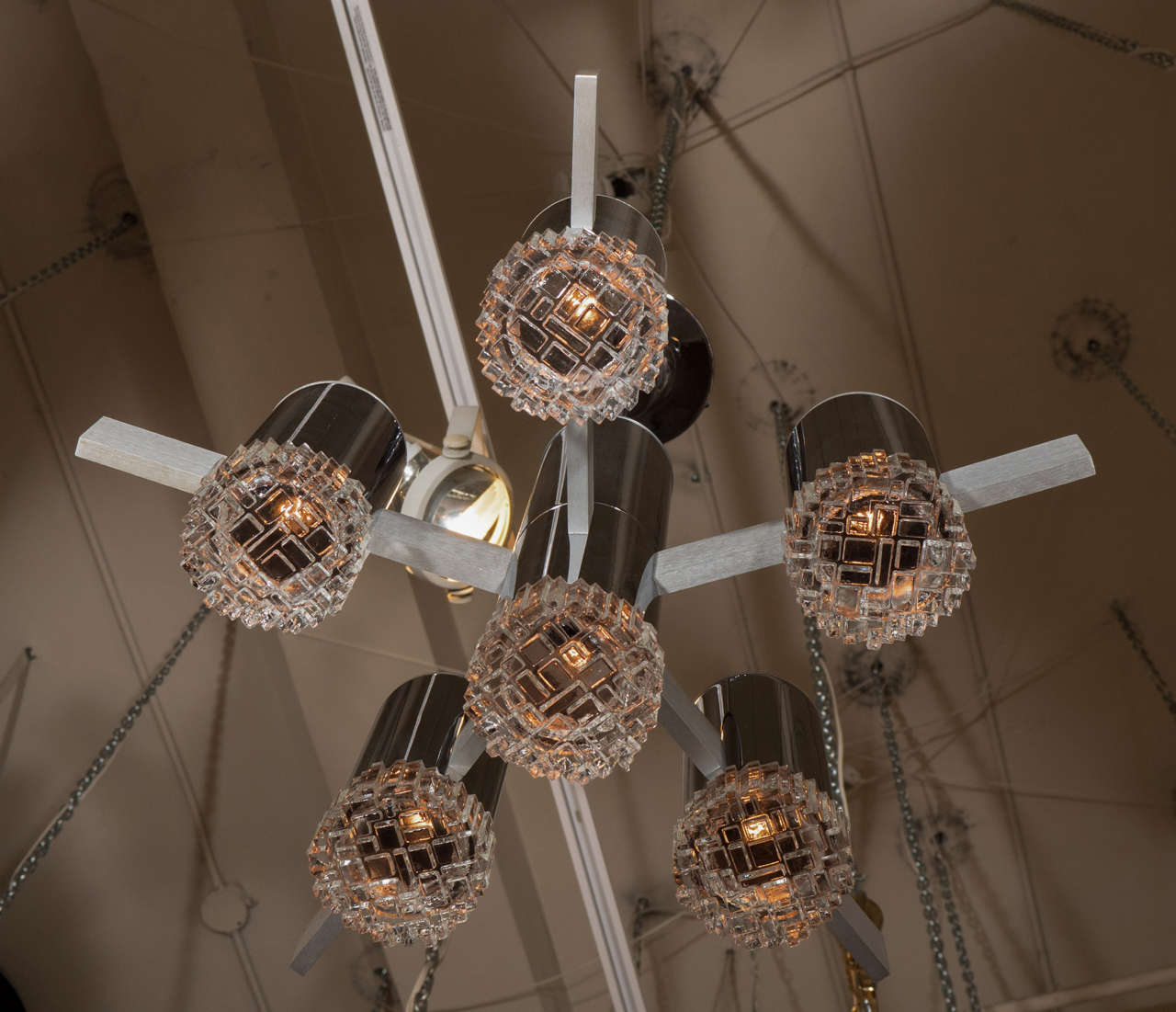 A sculptural 1970s chandelier by Italian lighting house Sciolari. Tubular socket covers, rod and ceiling canopy in a bright chrome finish complemented by the satin finish iron bar arms. Each of the six lights has a geometric design glass shade