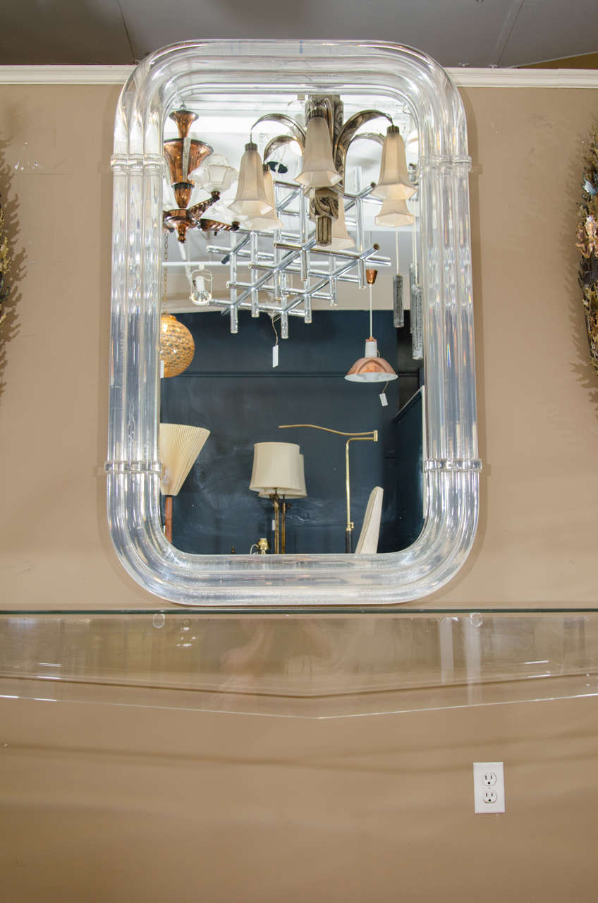 An Incredible 1970s Custom Designed Angular Lucite Console with Modern Cutout legs, glass top and a Monumental Substantial Well appointed Lucite wall-mounted mirror The Mirror is Constructed of Triple Layered Thick Curved Lucite which is Incredibly