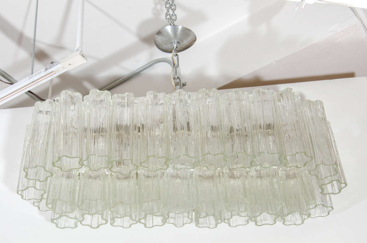 A Italian Modernist Chandelier by Camer with textured Tubular shaped Murano Glass Hanging Pendants .This two-tier design has large and smaller Clear Glass Hand blown Tronci Pendants that dangle from a Solid Chromed Metal frame. The chandelier