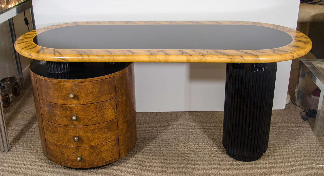 An Art Deco style desk with cylindrical bases and Faux tortoise top in the manner of Gilbert Rohde. Good vintage condition with age appropriate wear.  Some scratches to the top along with some chipping to the legs.