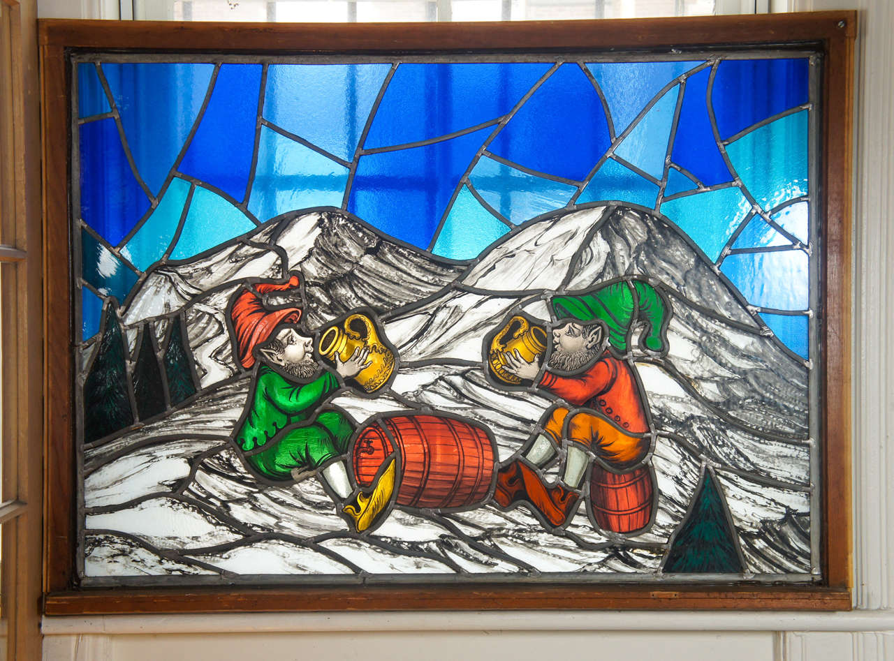 Delightful stained glass window of two elves or gnomes imbibing from a keg with flagons on a snowy landscape with evergreens under blue skies. Commissioned in Albany, New York