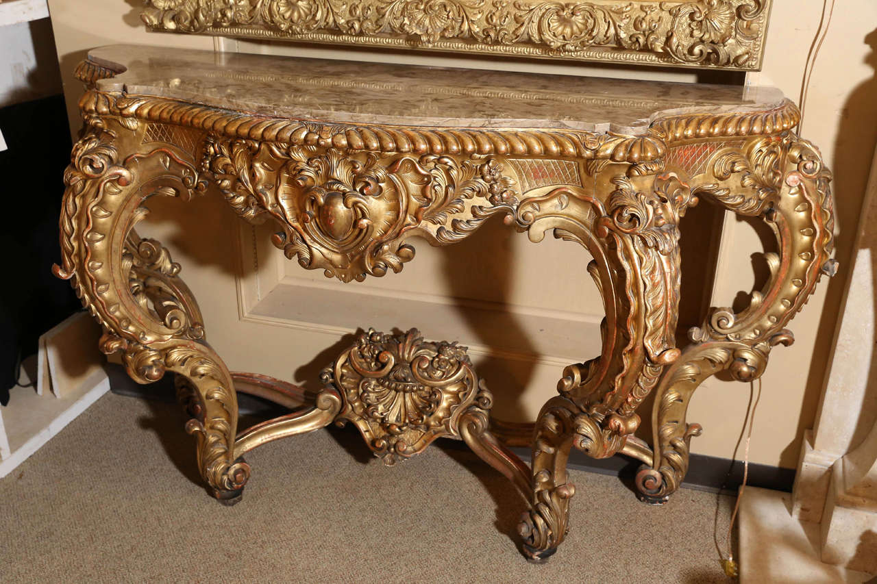 Italian giltwood baroque consoles with marble tops in taupe color
The pair having a highly carved apron with scrolls and cartouches
Shaped marble top within a gadroon edging
Foliage carved shield-centered frieze
