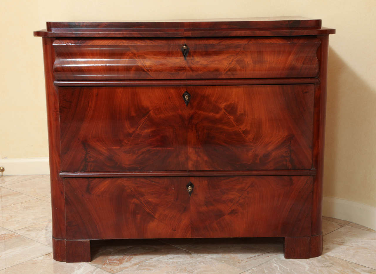 This piece beautifully exemplifies the Biedermeier's emphasis on using the timber's figure as ornament; here we see the rich and vibrant flame mahogany figure continuing over all three drawer fronts. The rectangular stepped top over an undulating