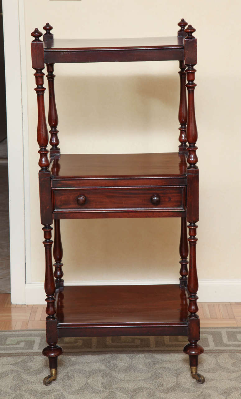 Regency mahogany three-tier etagere. With baluster-turned uprights and fitted with a frieze drawer; on brass caps and casters. Deep rich coloration.