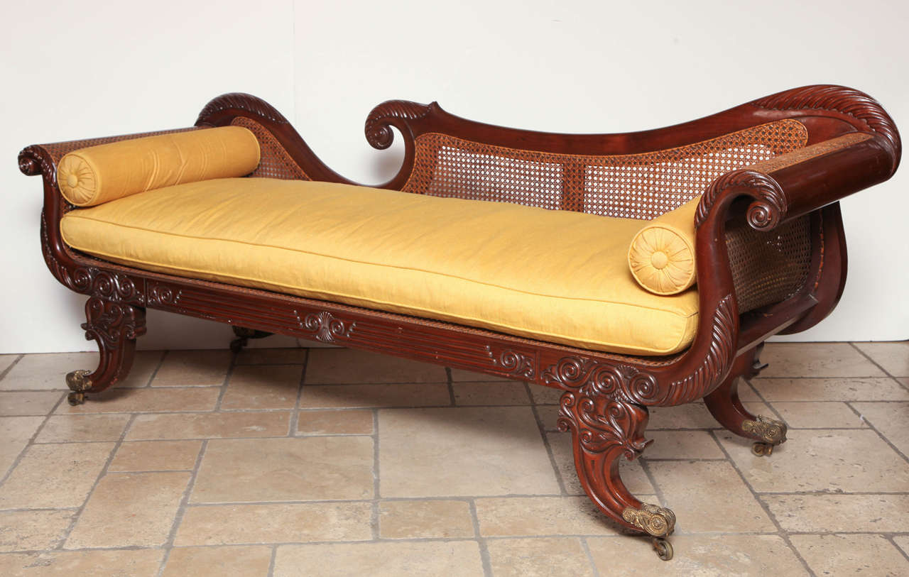 A fine Regency mahogany recamier with carved foliate and scroll decoration with hand-caned seat and back, fitted with loose cushions and blosters, the feet with foliate brass casters.