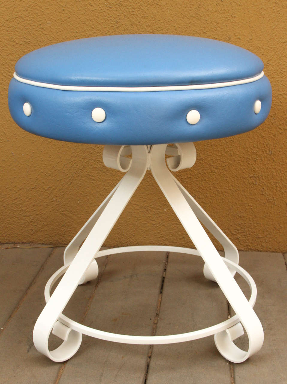 Three vintage indoor and outdoor stools with white iron bases and curled at the bottom and top of base. The seats have outdoor vinyl royal blue seats with white button detailing. The seats swivel.