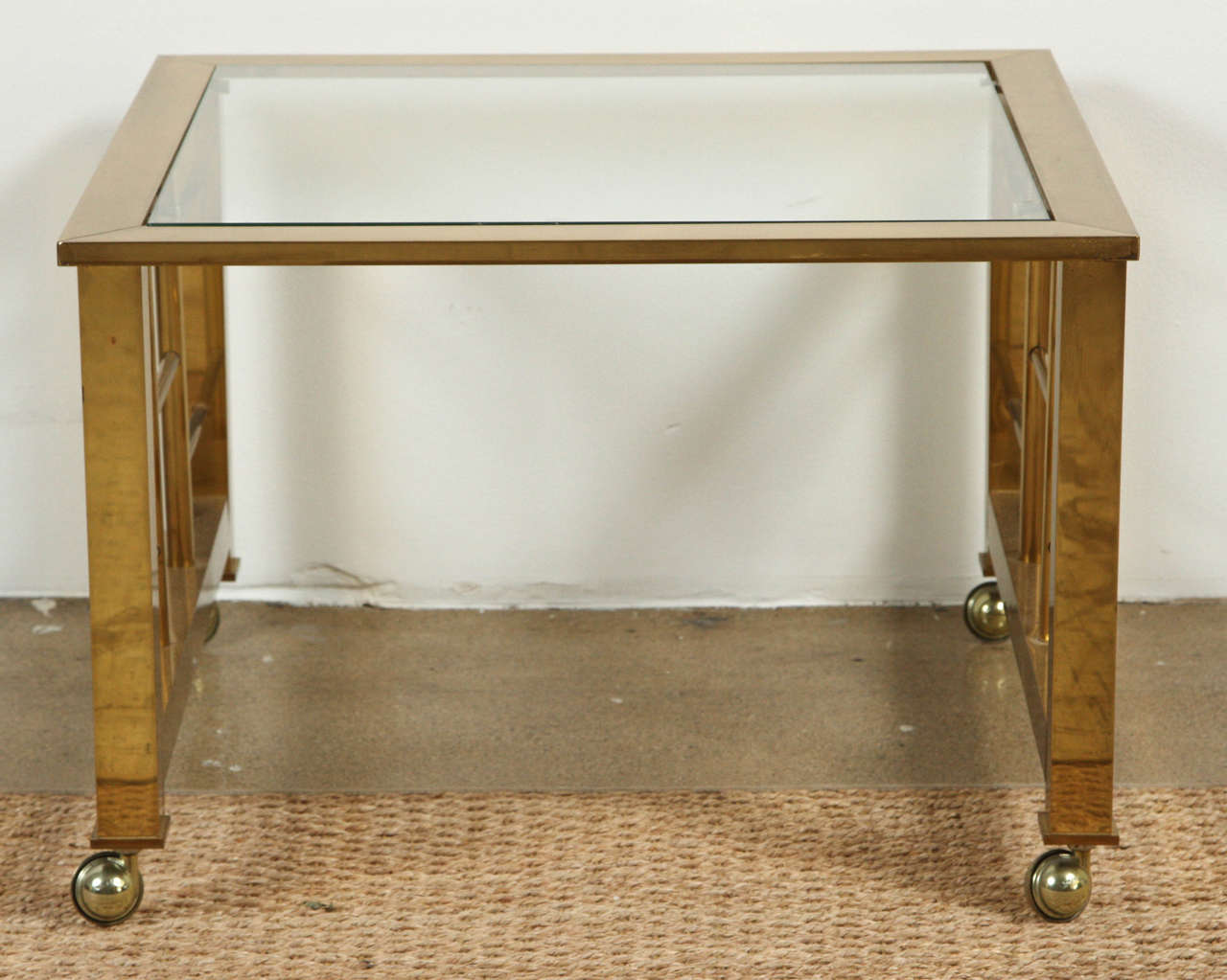 Perfect for the hard to find side table next to a chair and easy to move as it is on rollers. Brass and glass with brass cut-out on the sides shaped like squares.