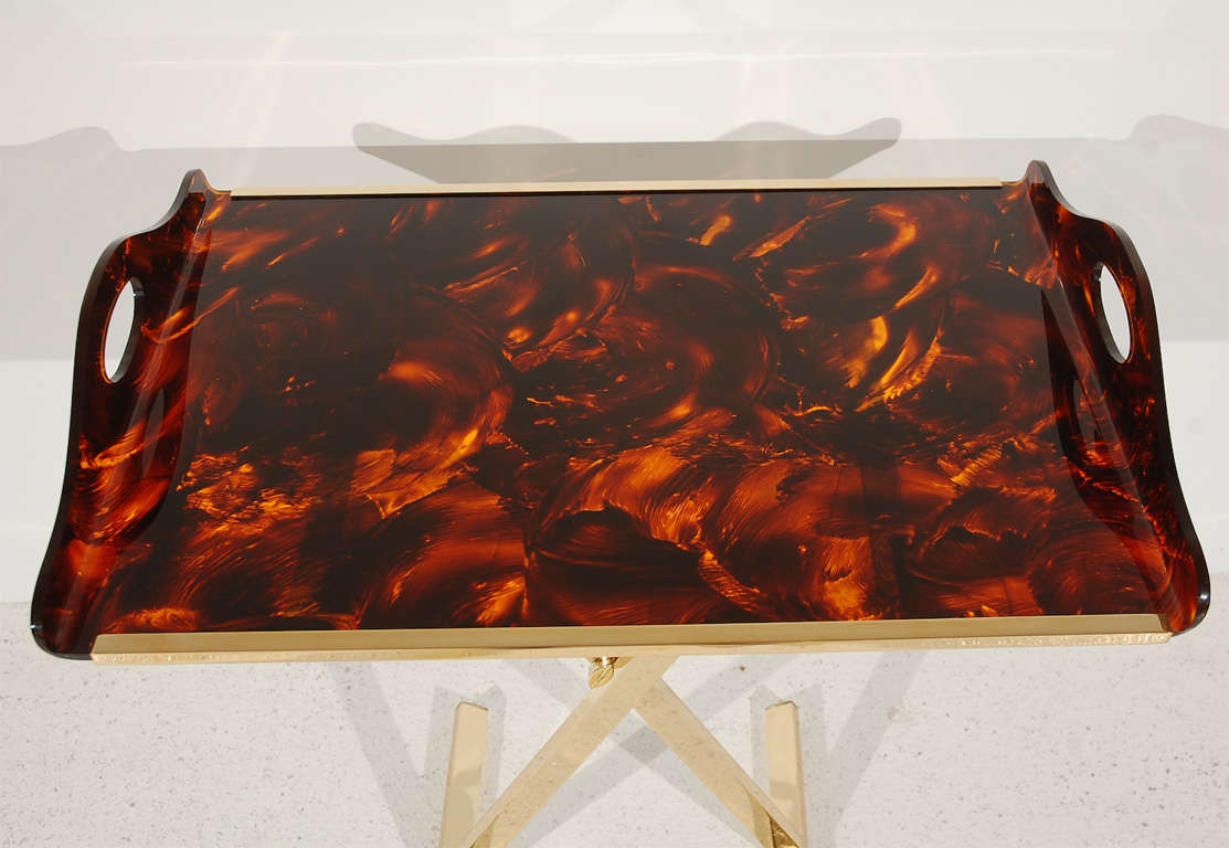 This chic piece features a faux tortoise shell handled acrylic tray with brass accents set atop an adjustable-height brass X base.