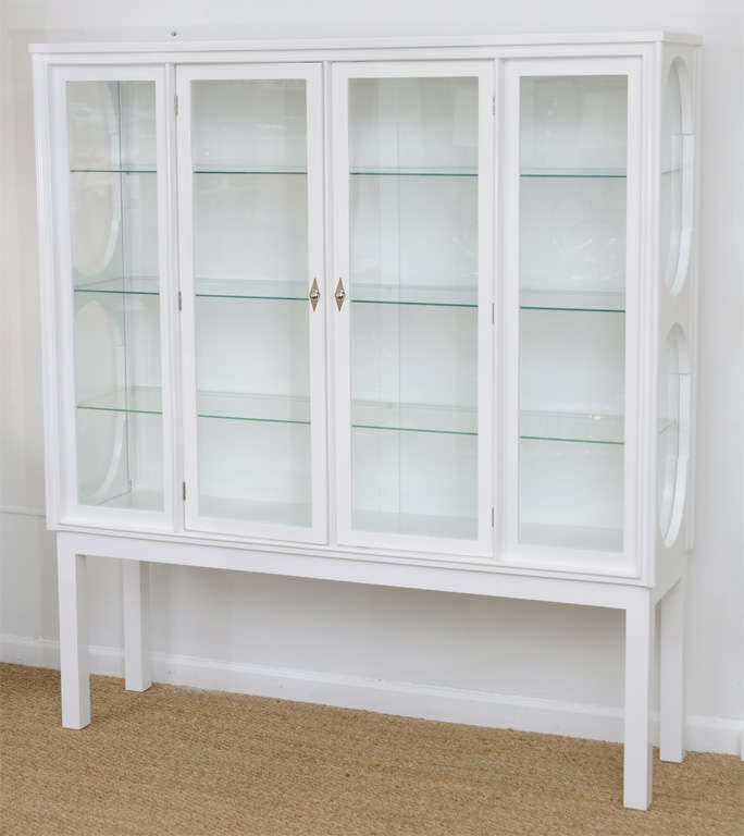 Tall standing glass front and sided cabinet with three interior glass shelves and one wood shelf. Sides have opera-style designed glass windows. Nickeled diamond back plates showcase nickeled door pulls on double french doors.