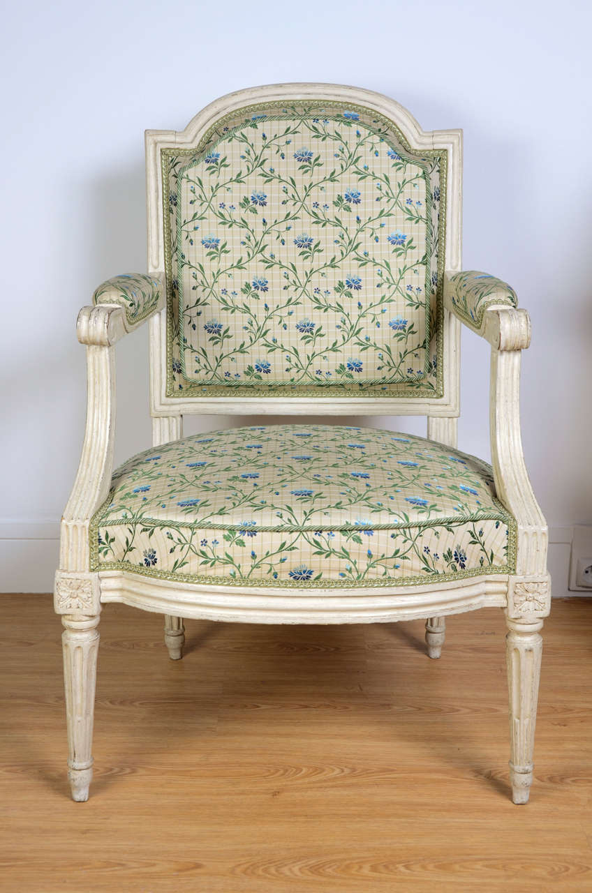 Pair of cream-painted molded wood Louis XVI armchairs. Curved backseat, fluted and spindled-shaped feet. Flower decor fabric. Stamped by Claude Chevigny, cabinetmaker master in 1768.