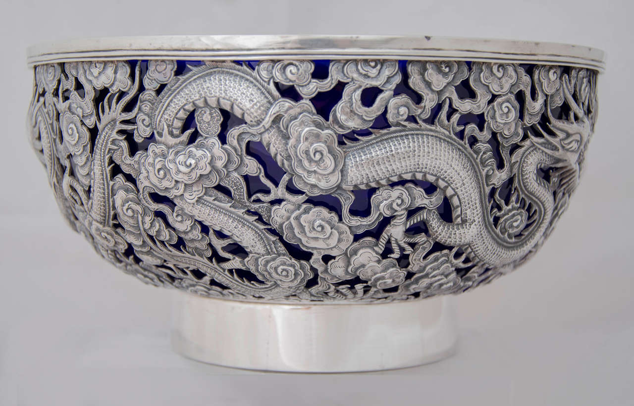 A large Chinese export silver bowl, beautifully pierced with two opposing dragons separated by a flaming pearl, and a third dragon breathing fire. 
The bowl has a blue glass liner.
