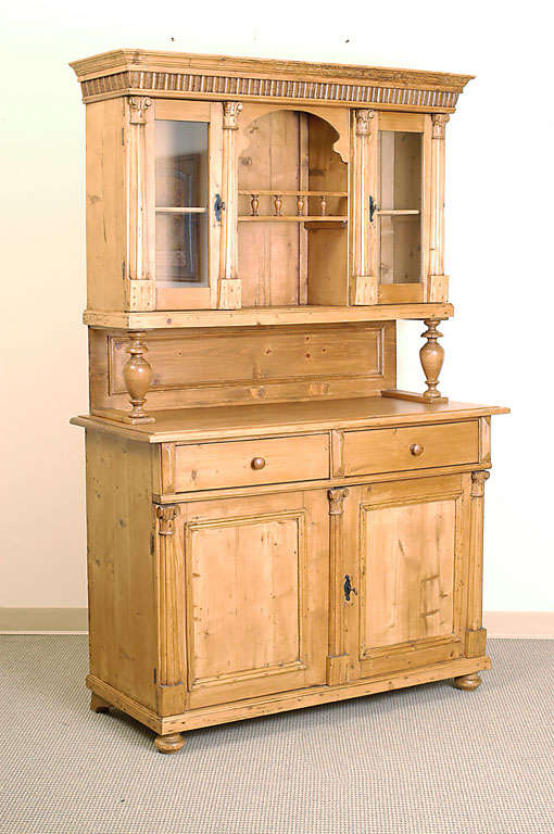 A handsome buffet or glazed dresser built in two parts. The upper section features two glazed doors flanking an open well with single shelf and gallery of turned spindles. Four split fluted balusters and an ornate crown enhance the decoration. A