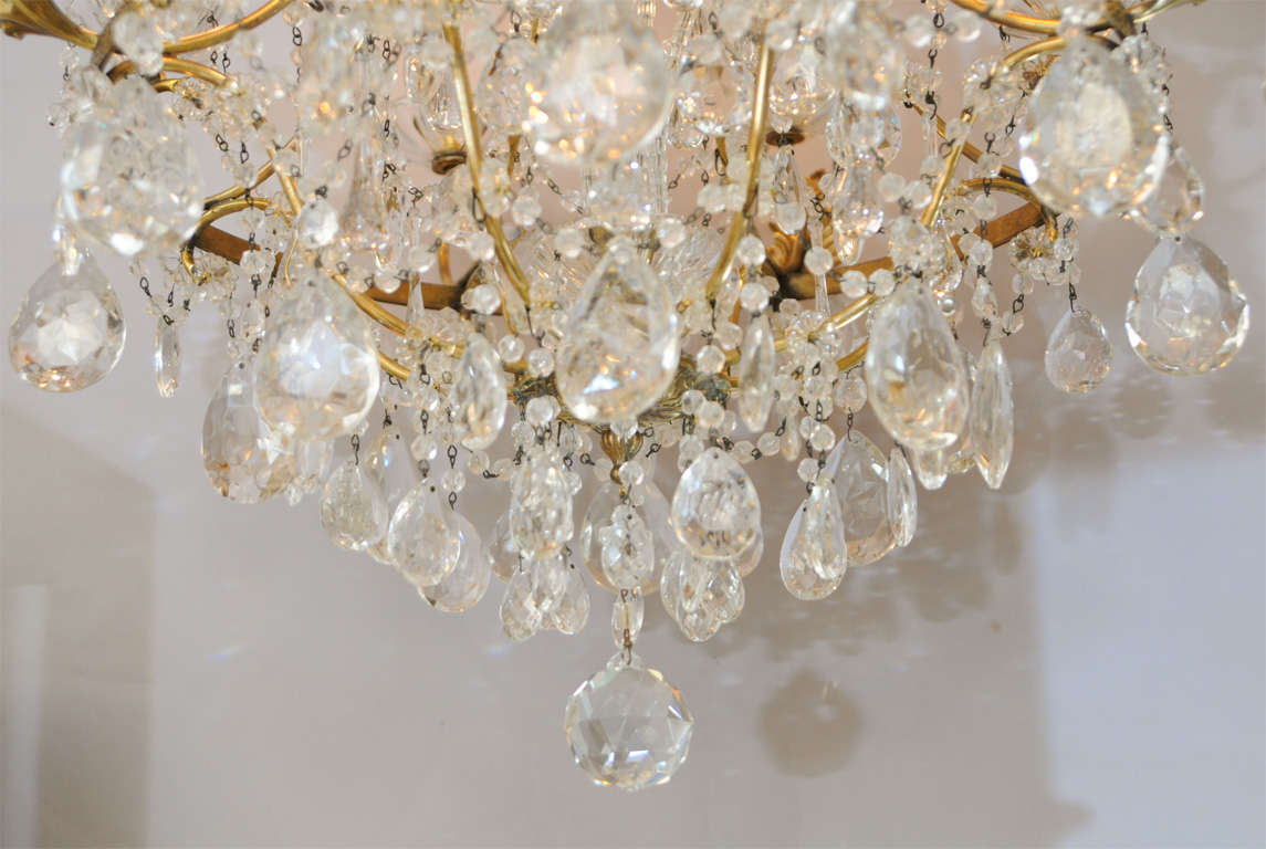 Chandelier, of gilt bronze, consisting of a finely chased ring suspended by shaped arms, finishing with leafy repousse cups holding eight lights in glass bobeches, the entire fixture draped in crystal strands, teardrops and prism drops.