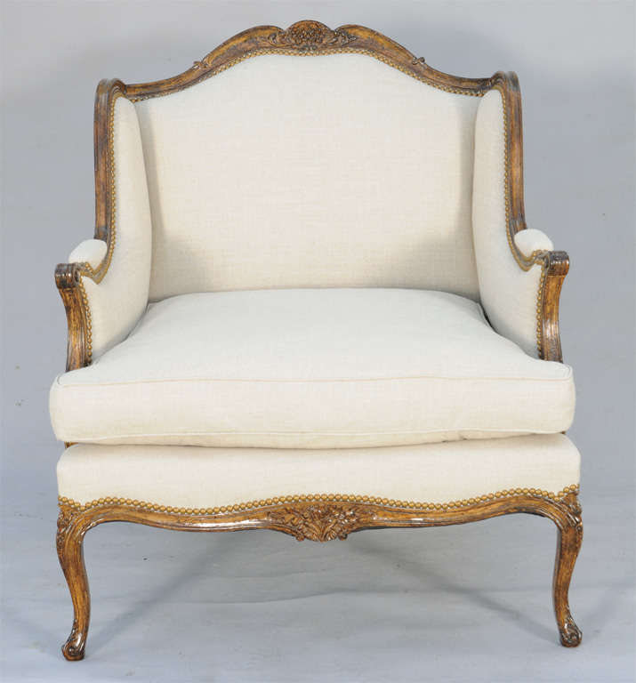 Pair of marquise bergere chairs, in Louis XV taste, each having a molded and channeled frame of walnut, it's bowed crestrail centered with carved flora, padded back and winged sides continue to padded elbow rests on sweeping terminals; loose cushion