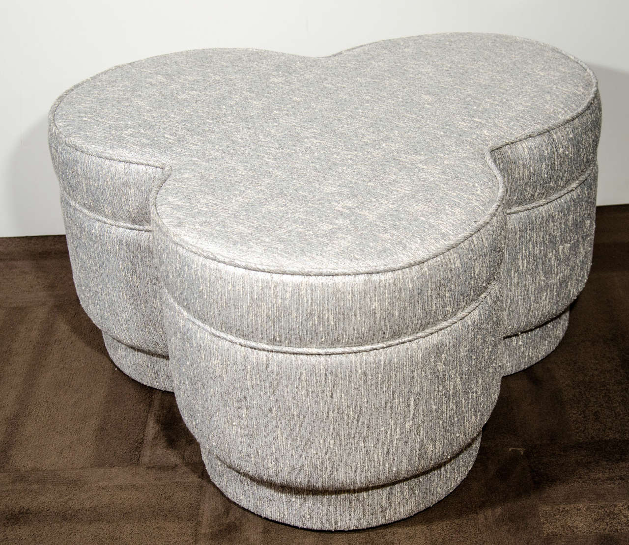 Hollywood era large-scale all upholstered ottoman/pouf with floating base detail and trefoil form. Newly upholstered in metallic ivory and platinum textured silk boucle. The ottoman features broad self welt detailed seams and firm seating . Great
