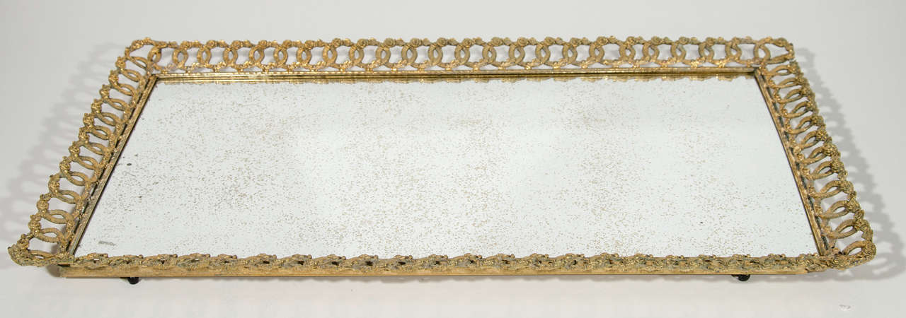 Elegant and unusual Art Deco mirrored tray with hand forged gilded metal frame.  The tray features intricate filigree link design with small roses/floral details.  The tray has a long rectangular form and has an antiqued mirror top with gold flecks