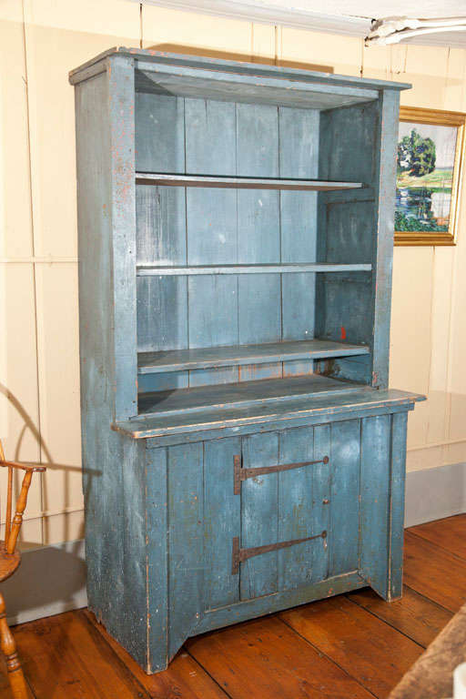 New England Stepback Cupboard with a 3 shelf top and strap hinged and batten lower door. With rosehead nail construction and 19th century dry blue painted surface this is a fine example of early new england high country furniture in a rarely found