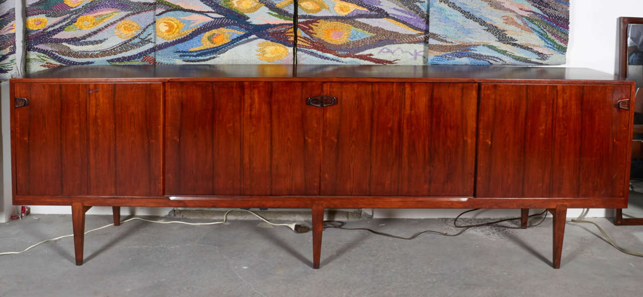 Vintage 1960s Extra Large Credenza

Very finely made eight feet long rosewood credenza with six legs by Rosengren Hansen of Denmark. The legs attach with a sharp trapezoidal detail that is echoed in the thinly carved pulls.  There are beautiful