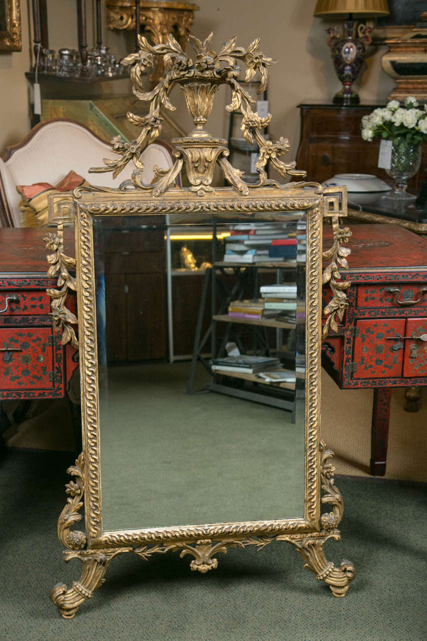 An 18th Century Italian Neoclassical giltwood, beveled looking glass mirror with carved and gilt floral, urn, cornucopia and Greek key motif.