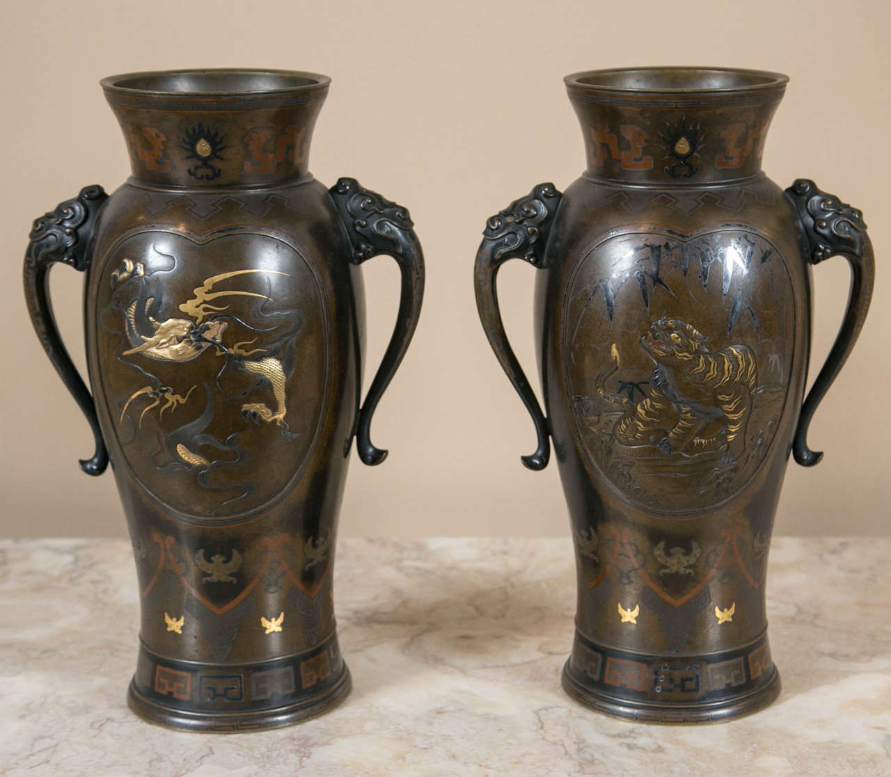 A stunning pair of 19th Century Meiji period, Japanese bronze and mixed metal vases having stylized elephant ear handles and high-relief gold and silver inlay.