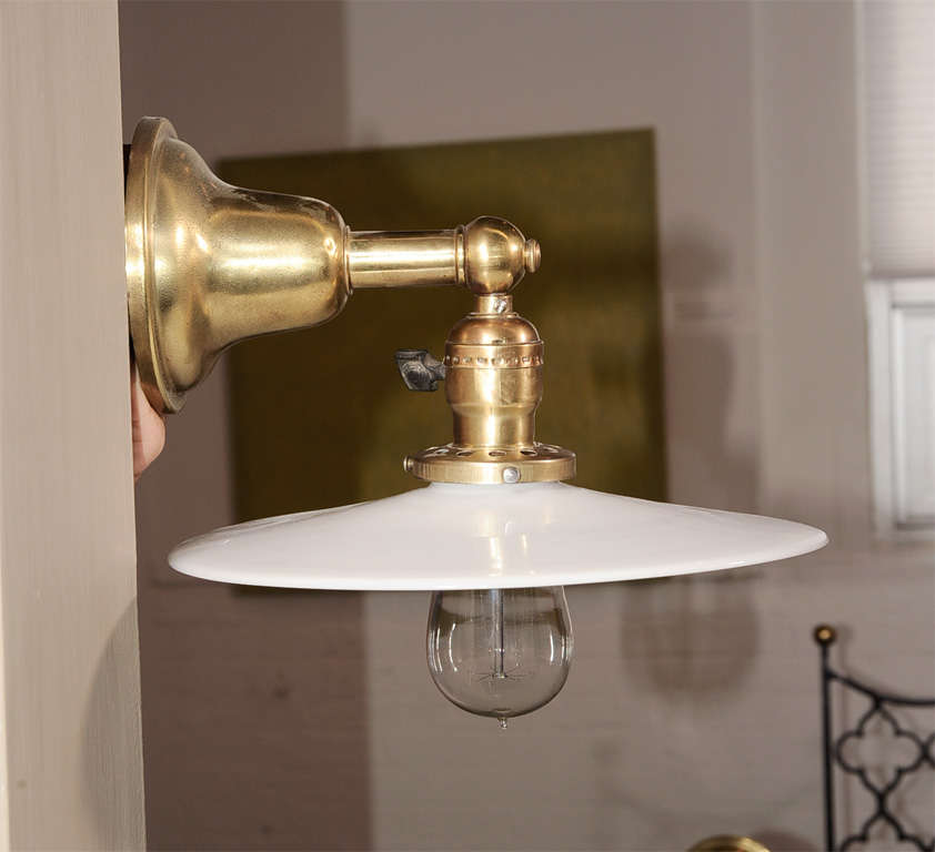 Pair of vintage brass wall lights / sconces with antique white milk glass disk shades.  USA, circa 1910.

Dimensions:
4.5 inch wall plate diameter (part that mounts to wall) 
9 inch depth overall/projection from wall (including shade)
8 inch