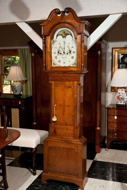 This tall case clock has a beautifully painted enamel face with a pair of turtle doves featured prominently at the center, indicating that this clock was probably a wedding or anniversary gift. In addition to the mahogany trim on the bonnet, the