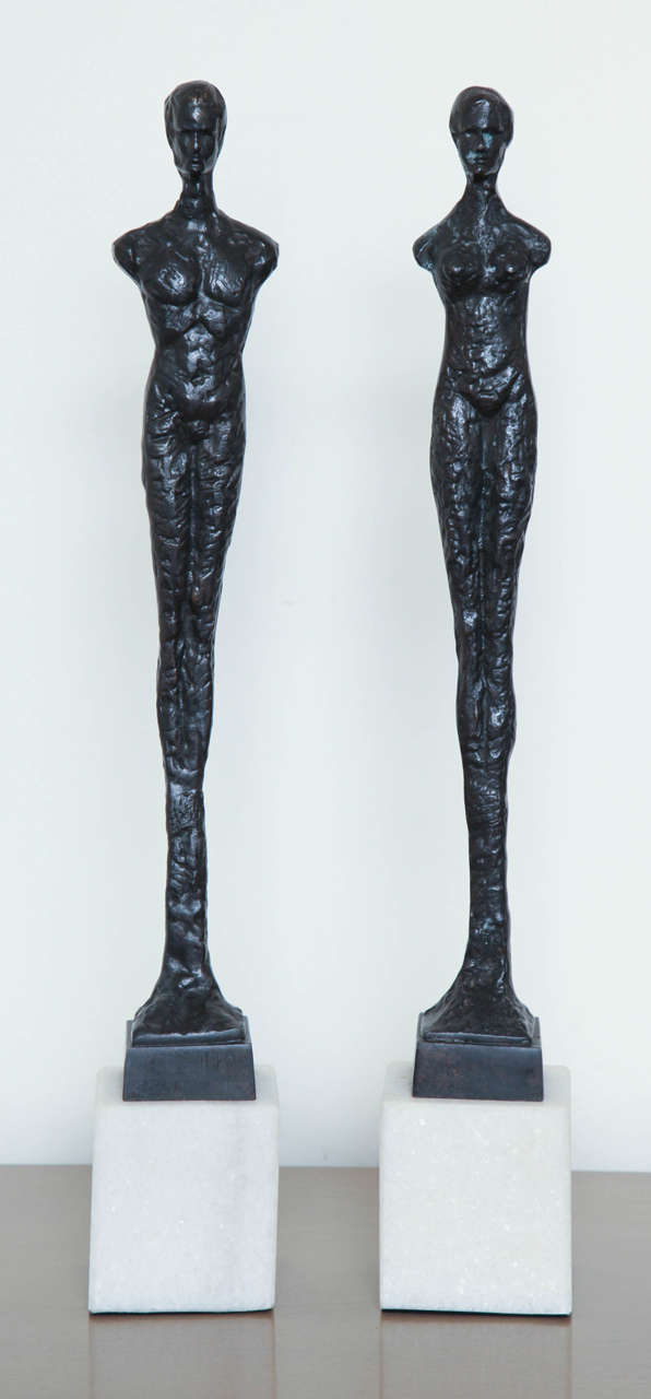 Pair of contemporary elongated bronze figurines mounted on white marble blocks in the style of Giacometti.