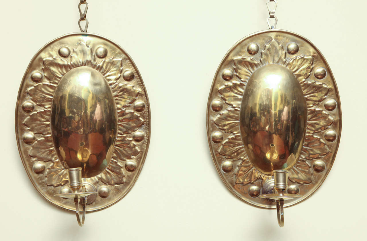 Very fine and rare pair of antique oval repousse brass sconces, the plain oval centers surrounded by leaf work and roundels in relief, and retaining the original shaped candle arms with cup and bobeche, Dutch or English, circa 1700.

Height: 11