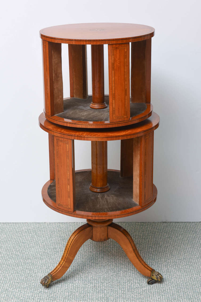 The top centered by a sunburst and with geometric banding, over two rotating tiers with leather-lined shelves and raised on a columnar support issuing three downswept legs terminating in brass paw feet and casters. Stunning lively figure nicely